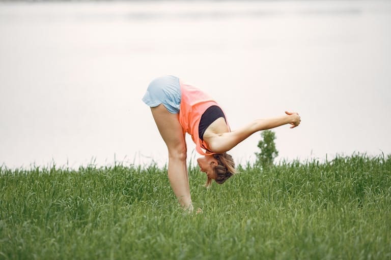 A woman in sports clothing practicing yoga and stretching in a grassy field.