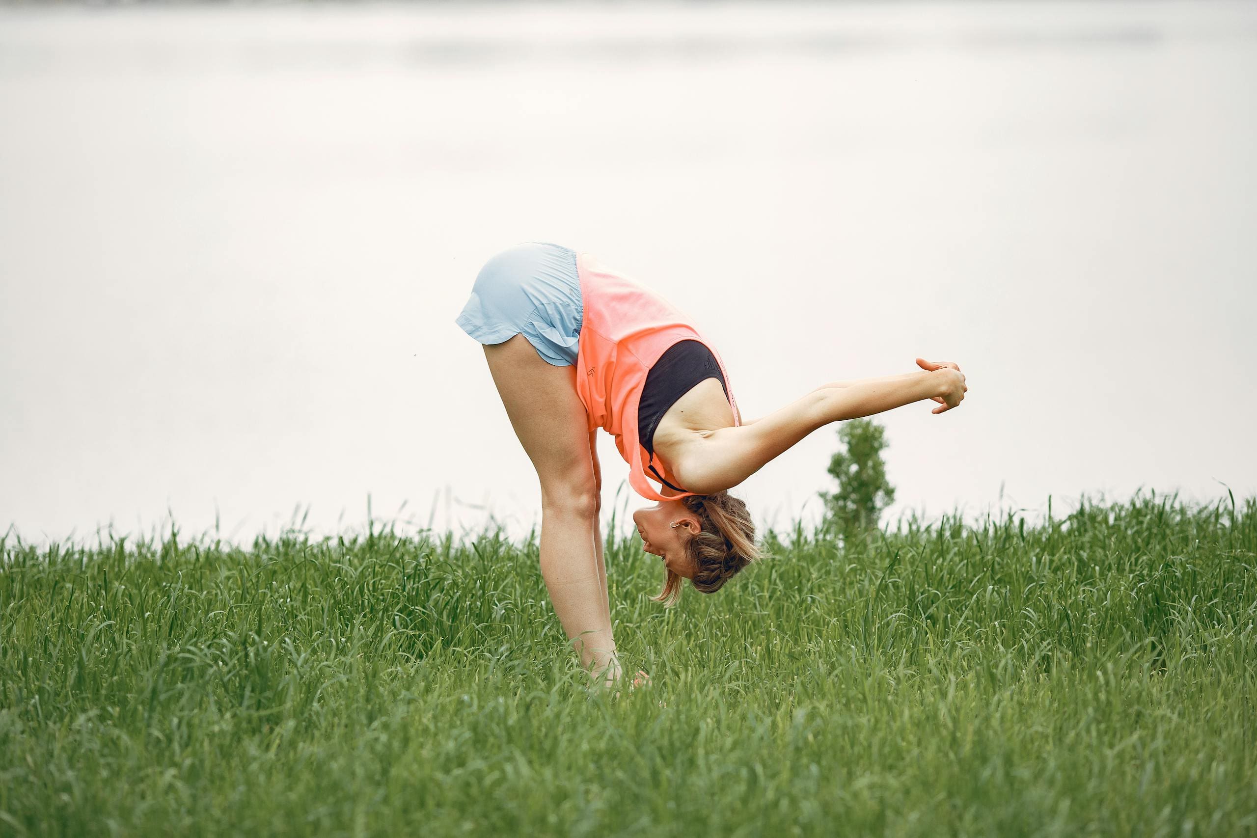 A woman in sports clothing practicing yoga and stretching in a grassy field.