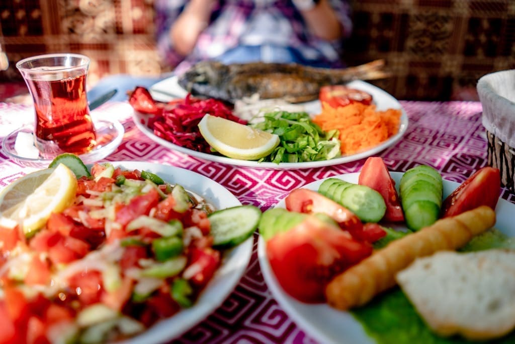 Close-up of a Mediterranean meal with grilled fish, fresh salad, and tea on a restaurant table.